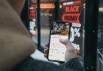 Anonymer Konsument mit Smartphone steht vor einem Black Friday-Schaufenster