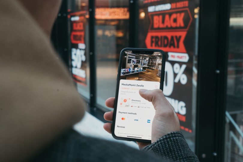 Anonymer Konsument mit Smartphone steht vor einem Black Friday-Schaufenster
