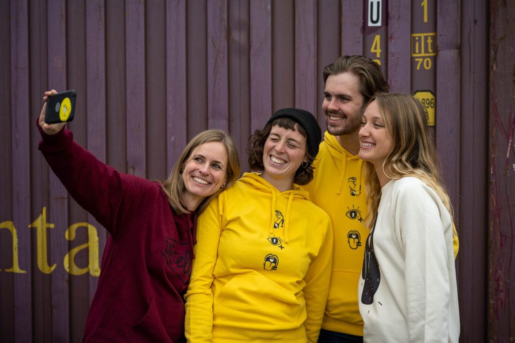 Vier WEtell-Mitarbeiter machen einen Selfie vor einem Container